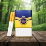 ซองบุหรี่ 555 STATE EXPRESS Original และมวนบุหรี่ วางบนโต๊ะไม้ฉากหลังสวนสีเขียว