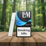 ซองบุหรี่ L&M Storm 7.1 สีดำดีไซน์แถบสีฟ้า และมวนบุหรี่ วางบนโต๊ะไม้ฉากหลังป่าสีเขียว