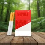 ซองบุหรี่ Napoli Red Special สีแดงเข้มและขาว วางคู่กับมวนบุหรี่บนโต๊ะไม้ในบรรยากาศป่าไม้ธรรมชาติ