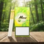 ซองบุหรี่ Mars Honeydew สีเขียวเหลืองสดใส วางบนโต๊ะไม้พร้อมมวนบุหรี่ ในบรรยากาศสวนป่าสีเขียว
