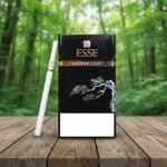 บุหรี่ ESSE Golden Leaf เอสเซ่ โกลเด้น ลีฟ แพ็กเกจสีดำทอง วางบนโต๊ะไม้ในสวนป่า