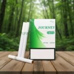 ซองบุหรี่ Journey Green และมวนบุหรี่ วางบนโต๊ะไม้ในบรรยากาศป่าสีเขียว