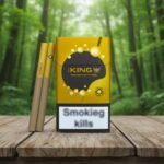 ซองบุหรี่ The King Mango สีทองตัดดำ วางคู่กับมวนบุหรี่บนโต๊ะไม้กลางป่า