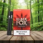 ซองบุหรี่ Black Fox Strawberry สีแดงลายหน้าสุนัขจิ้งจอก วางคู่กับมวนบุหรี่สีดำสนิทบนโต๊ะไม้ฉากหลังป่าเขียวขจี