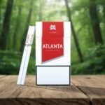 ซองบุหรี่ Atlanta Super Slims Red สีแดงขาว วางคู่กับมวนบุหรี่แบบสลิมบนพื้นไม้ ฉากหลังเป็นป่าสีเขียว