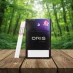 ซองบุหรี่ Oris Nano Crush Blueberry สีดำดีไซน์ล้ำสมัย พร้อมมวนขนาดนาโนวางบนพื้นโต๊ะไม้และฉากหลังป่า