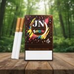 ซองบุหรี่ JN Show และมวนบุหรี่ วางบนโต๊ะไม้ท่ามกลางบรรยากาศสวนป่าสีเขียว