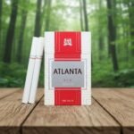 ซองบุหรี่ Atlanta Red Premium สีขาวแถบแดงวางคู่กับมวนบุหรี่สีขาวบนโต๊ะไม้กลางป่า
