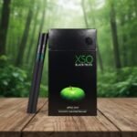 ซองบุหรี่ XSO Apple Mint สีดำพรีเมียม วางบนโต๊ะไม้ฉากหลังเป็นป่าสีเขียว
