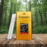 ซองบุหรี่ Zumerret Gold สีทองหรูหรา พร้อมเทคโนโลยี Auto Lock วางบนโต๊ะไม้ฉากหลังป่าไม้สีเขียว