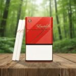 ซองบุหรี่ Davidoff Supreme สีแดงดีไซน์ลวดลายจุดสุดหรู พร้อมมวนขนาด Magnum วางบนโต๊ะไม้ฉากหลังป่า