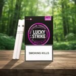 บุหรี่ Lucky Strike Purple ซองสีดำโลโก้สีม่วงแบบเม็ดบีบ วางบนโต๊ะไม้ฉากหลังป่าสีเขียว