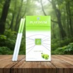 บุหรี่ Platinum Seven Green Apple ซองสีขาวเขียวลายรูปแอปเปิ้ล วางบนโต๊ะไม้ฉากหลังป่าธรรมชาติ