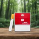 บุหรี่ Dunhill International ซองแข็งสีแดงดีไซน์เรียบหรู วางคู่กับมวนบุหรี่บนโต๊ะไม้ฉากหลังป่าธรรมชาติ