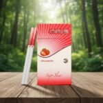 บุหรี่ Oris Strawberry Super Slims ซองสีชมพูแดงรูปสตรอเบอร์รี่ วางบนโต๊ะไม้ฉากหลังป่าไม้ธรรมชาติ