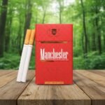 บุหรี่ Manchester Royal Red ซองสีแดงลายจุดพรีเมียม พร้อมมวนบุหรี่ วางบนโต๊ะไม้ฉากหลังป่าสีเขียว