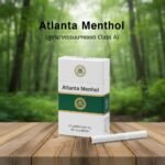 ซองบุหรี่ Atlanta Green Menthol สีขาวแถบเขียว วางบนโต๊ะไม้ฉากหลังเป็นป่าธรรมชาติสีเขียว