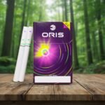 ซองบุหรี่ Oris Twin Sense Berry Mix สีม่วงดีไซน์ทันสมัย วางบนโต๊ะไม้ฉากหลังเป็นป่าธรรมชาติ