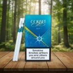 บุหรี่ Corset Deux ซองสีฟ้าเมทัลลิก ดีไซน์หรูหรา วางคู่กับมวนบุหรี่ซูเปอร์สลิมบนโต๊ะไม้ฉากหลังป่า