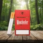 ซองบุหรี่ Manchester Royal Red สีแดงเข้มพื้นผิวลายจุดสุดหรู วางบนโต๊ะไม้กลางธรรมชาติ พร้อมมวนบุหรี่ก้นกรองสีน้ำตาลทอง