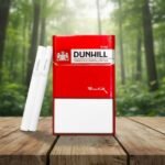 บุหรี่ Dunhill Red 10mg ซองแข็งสีแดงดีไซน์เรียบหรู วางคู่กับมวนบุหรี่สีขาวก้นกรอง Flow Filter บนโต๊ะไม้ท่ามกลางธรรมชาติ