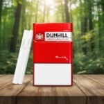 บุหรี่ Dunhill Red 10mg ซองสีแดงพรีเมียมพร้อมมวนบุหรี่ วางบนโต๊ะไม้ในบรรยากาศป่าไม้ธรรมชาติ