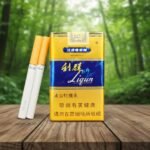 ซองบุหรี่ Liqun Gold สีทองคาดน้ำเงินพร้อมมวนบุหรี่ วางบนโต๊ะไม้ท่ามกลางพื้นหลังป่าไม้ธรรมชาติ