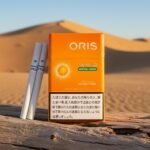 ซองบุหรี่ Oris Switch Menthol Orange สีส้มสดใส วางบนขอนไม้ฟอกขาวกลางทะเลทราย พร้อมมวนซุปเปอร์สลิม