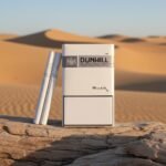 ซองบุหรี่ Dunhill White 1mg ดีไซน์เรียบหรูสีขาว วางบนขอนไม้ท่ามกลางวิวทะเลทรายสีทอง