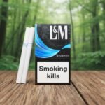 ซองบุหรี่ L&M Storm 7.1 สีดำดีไซน์ทันสมัยวางบนโต๊ะไม้ พร้อมพื้นหลังป่าสีเขียว