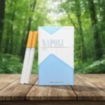 บุหรี่ Napoli Blue Special ซองสีขาวฟ้าดีไซน์มินิมอล พร้อมมวนบุหรี่ วางบนโต๊ะไม้ท่ามกลางธรรมชาติ